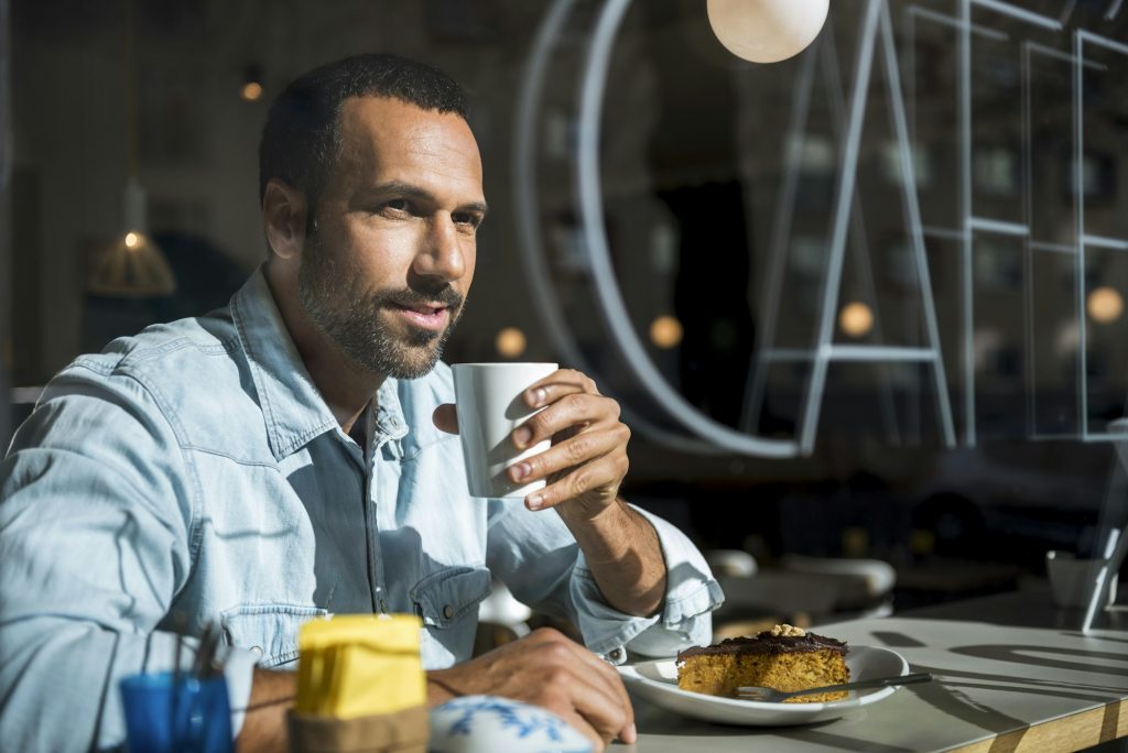 Smiling man drinking coffee and eating cake in a cafe