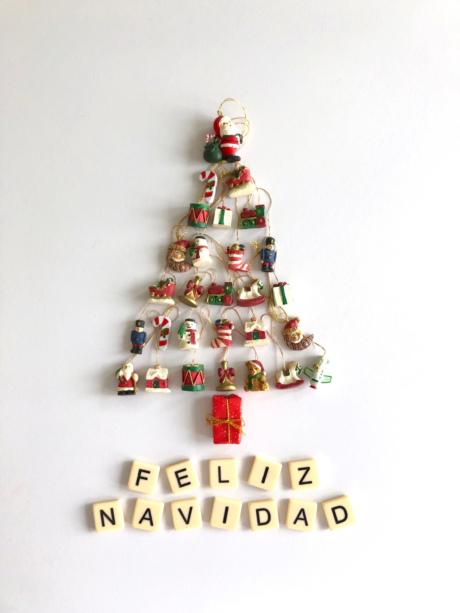 Christmas tree flat lay made with tiny ornaments & Merry Christmas written in Spanish Feliz Navidad